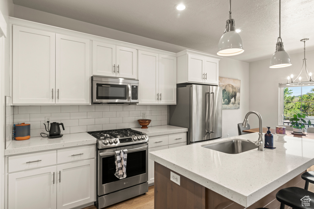 Kitchen featuring white cabinetry, hanging light fixtures, stainless steel appliances, a kitchen island with sink, and backsplash