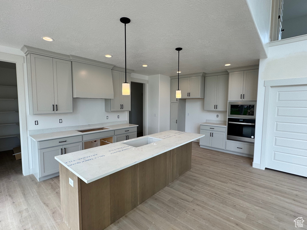 Kitchen featuring light wood-type flooring, a center island, custom range hood, gray cabinetry, and stainless steel appliances