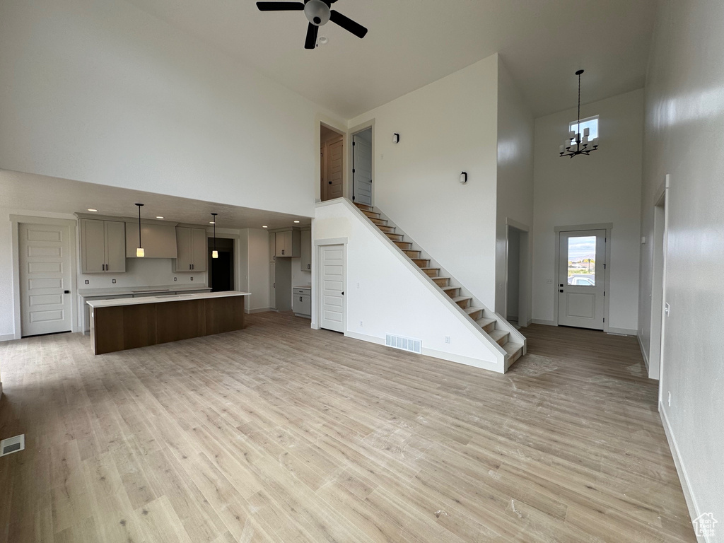 Unfurnished living room with ceiling fan with notable chandelier, a high ceiling, and light hardwood / wood-style flooring