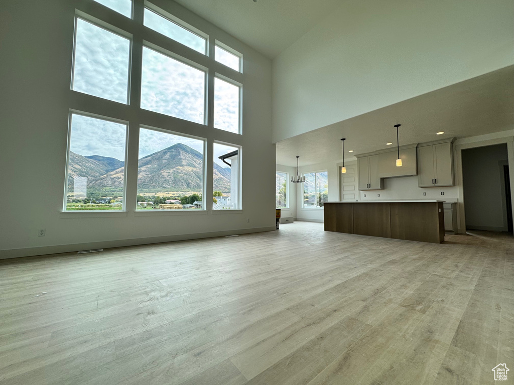 Unfurnished living room with a notable chandelier, light wood-type flooring, plenty of natural light, and a high ceiling