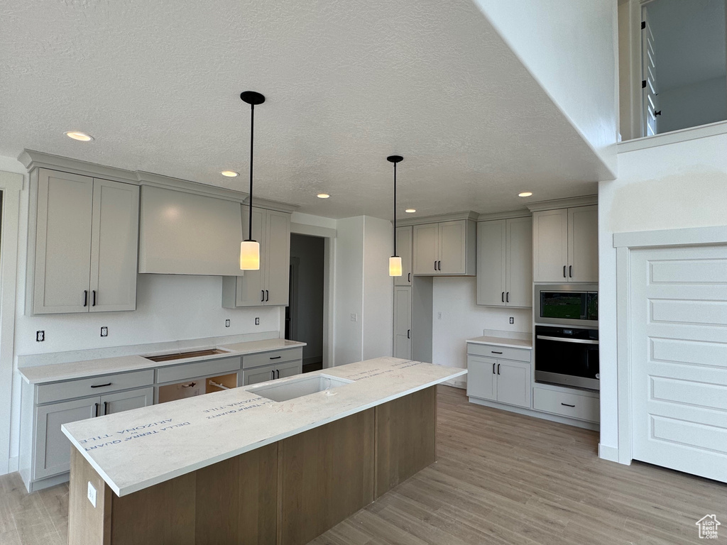 Kitchen featuring light hardwood / wood-style floors, a kitchen island, pendant lighting, gray cabinets, and cooktop