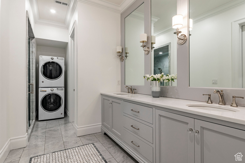 Bathroom featuring tile flooring, stacked washing maching and dryer, double vanity, and ornamental molding