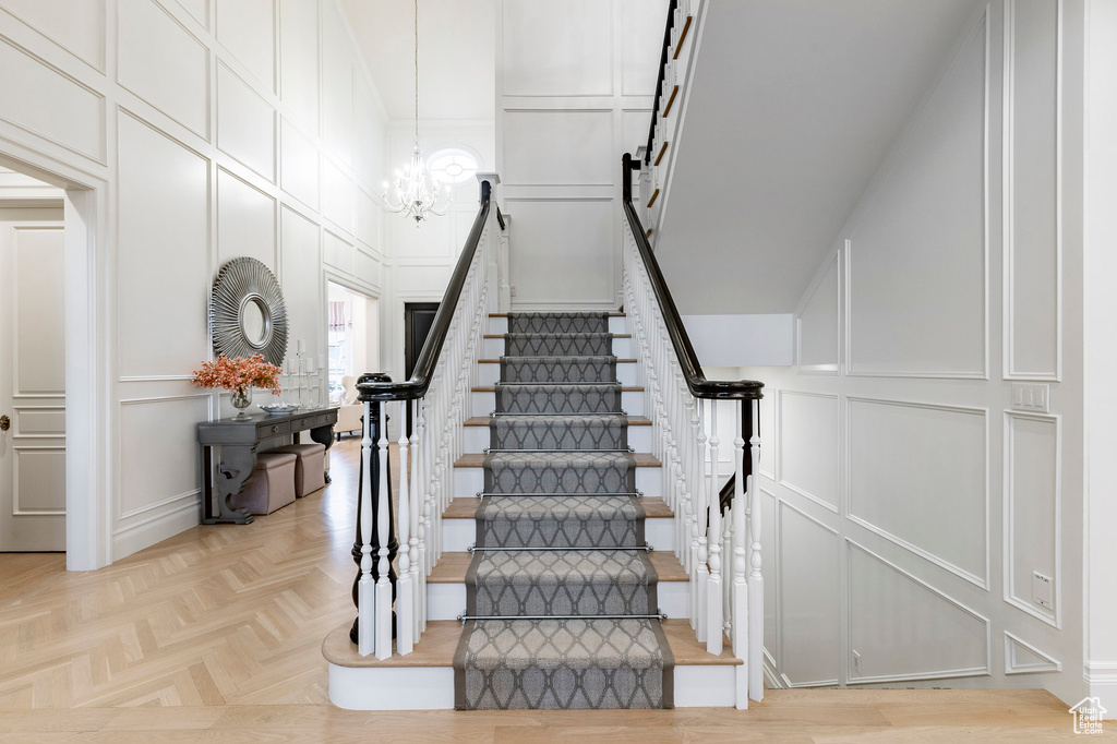 Staircase with a notable chandelier, a towering ceiling, and light parquet flooring