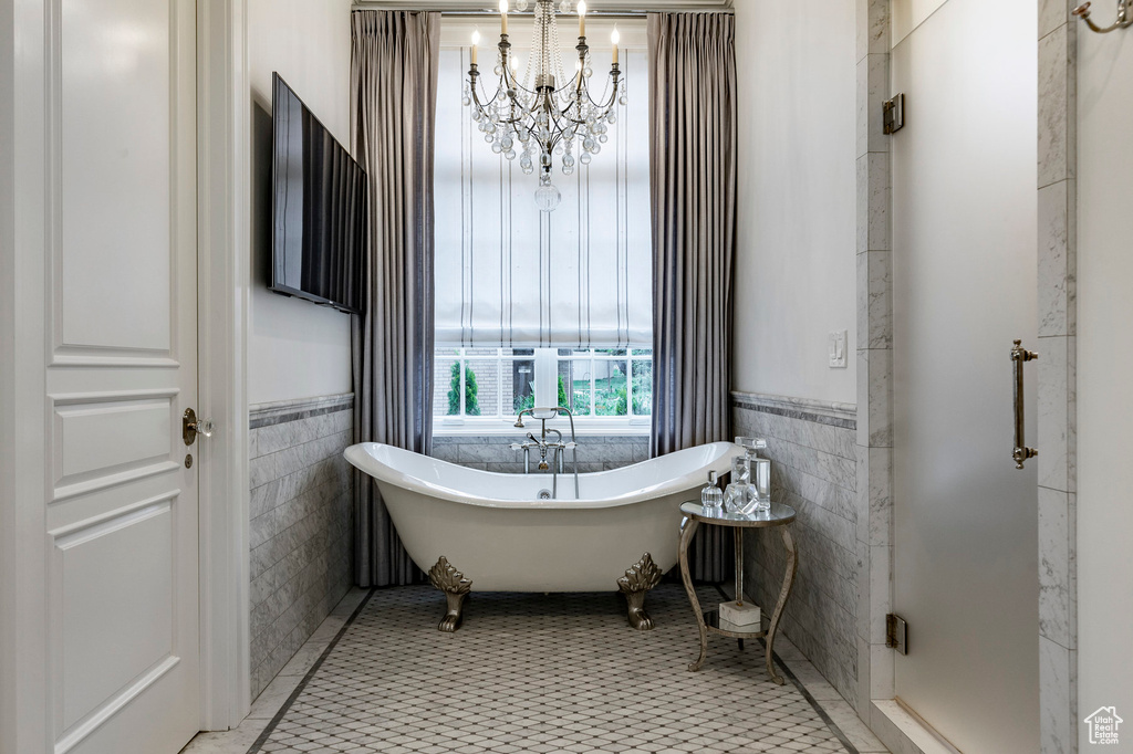 Bathroom featuring a washtub, tile flooring, a chandelier, and tile walls