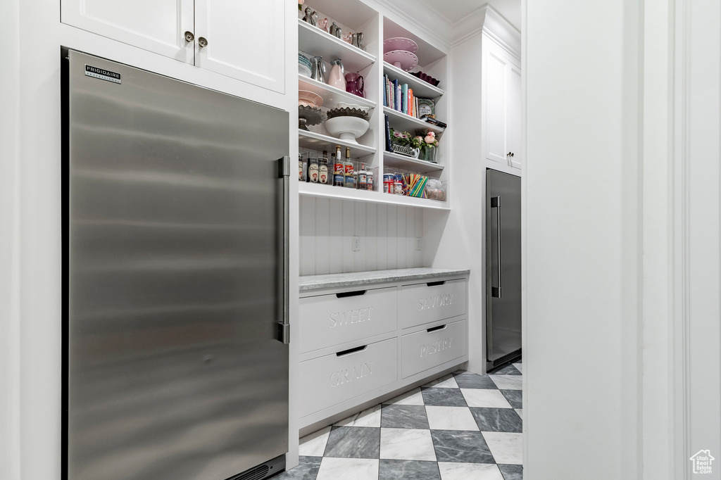 Interior space with stainless steel fridge, white cabinetry, and light tile floors