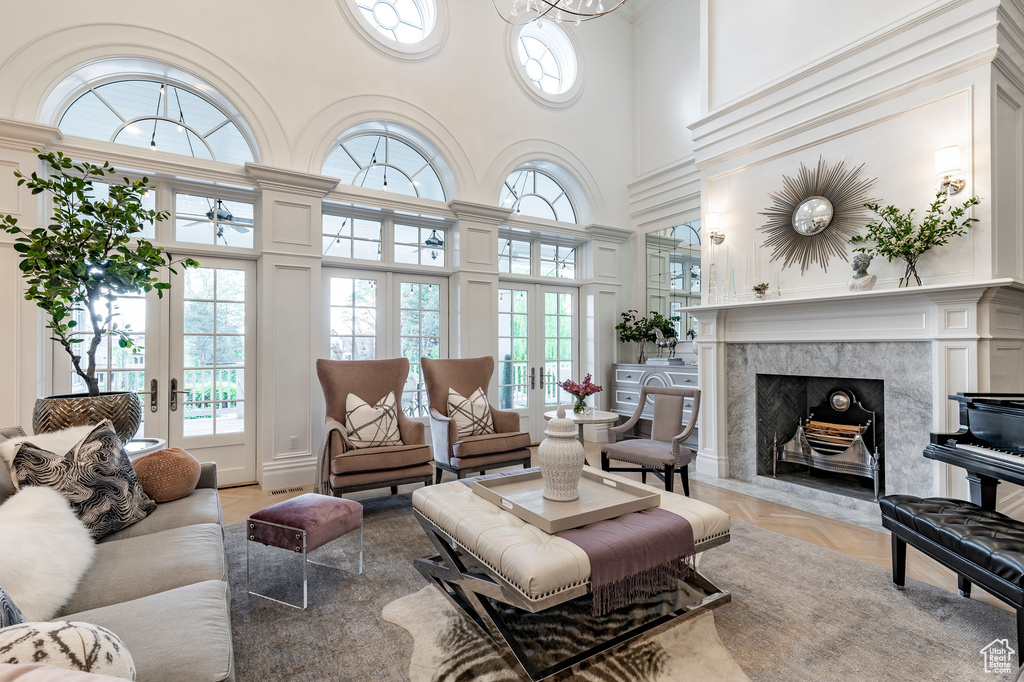 Living room with a high ceiling, a high end fireplace, french doors, and light parquet flooring