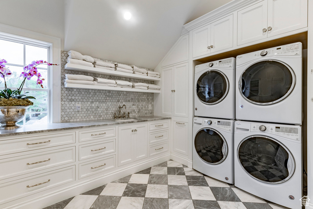 Washroom with a wealth of natural light, stacked washer / drying machine, sink, and light tile floors