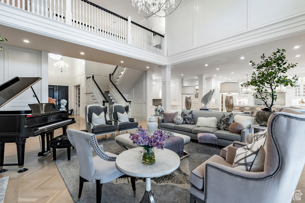 Living room featuring a high ceiling, light parquet flooring, a chandelier, and ornate columns