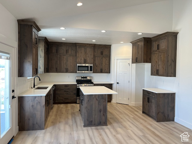 Kitchen with stainless steel appliances, a kitchen island, dark brown cabinetry, light hardwood / wood-style floors, and lofted ceiling