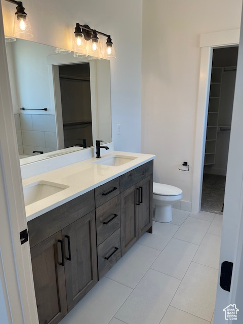 Bathroom featuring toilet, tile patterned flooring, and dual bowl vanity