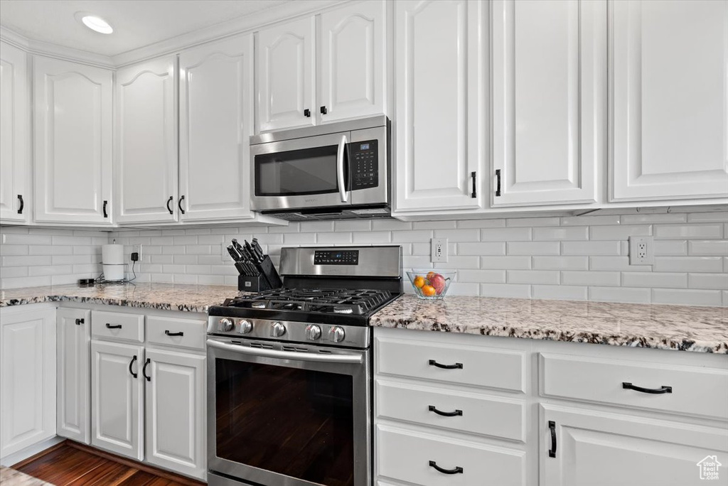 Kitchen featuring dark hardwood / wood-style flooring, backsplash, light stone countertops, white cabinets, and appliances with stainless steel finishes