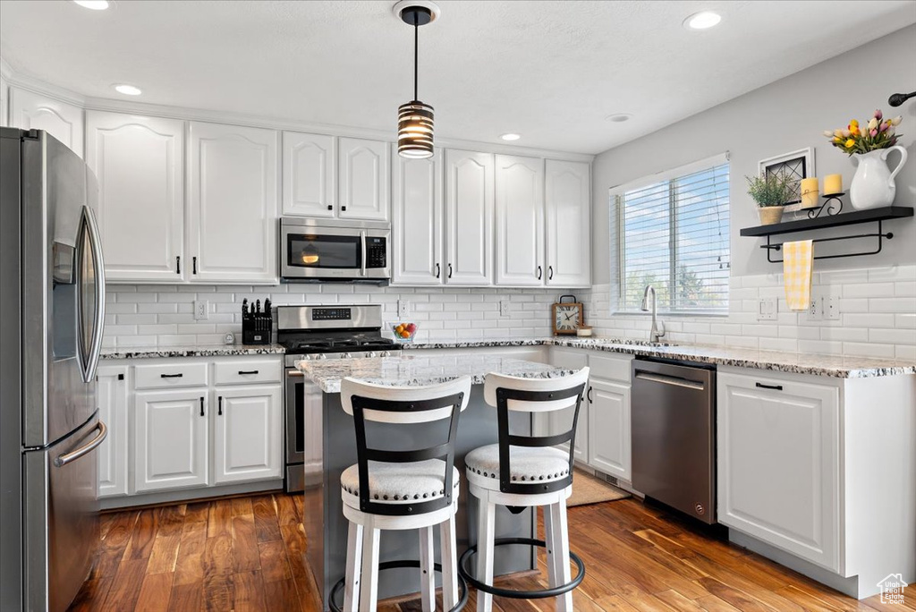 Kitchen with white cabinetry, a kitchen island, appliances with stainless steel finishes, hardwood / wood-style flooring, and tasteful backsplash