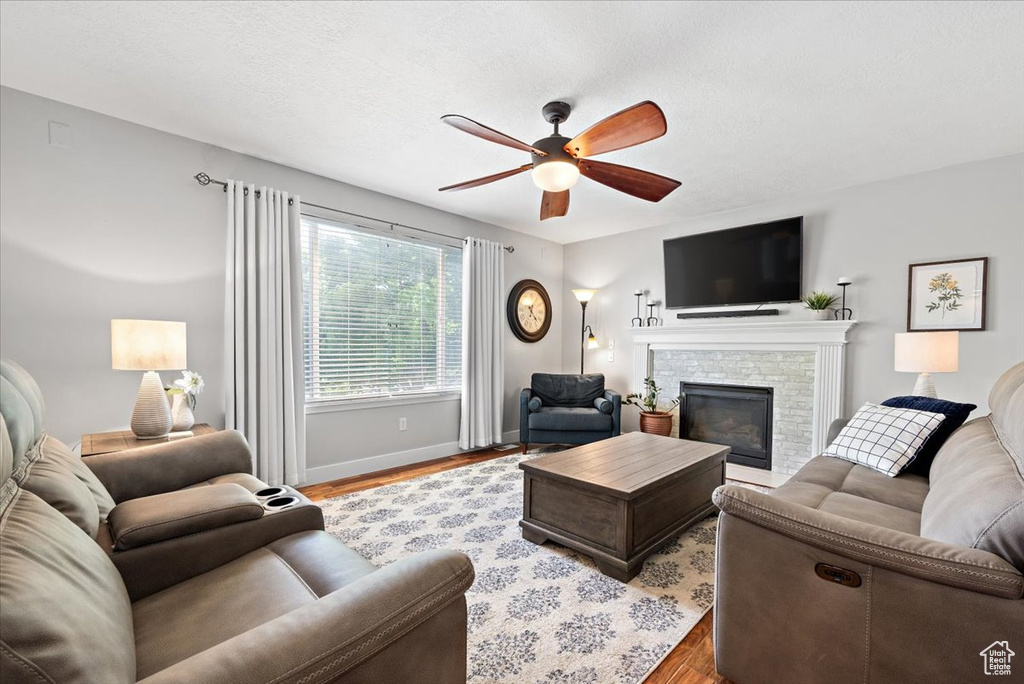 Living room featuring ceiling fan, a stone fireplace, and light hardwood / wood-style flooring