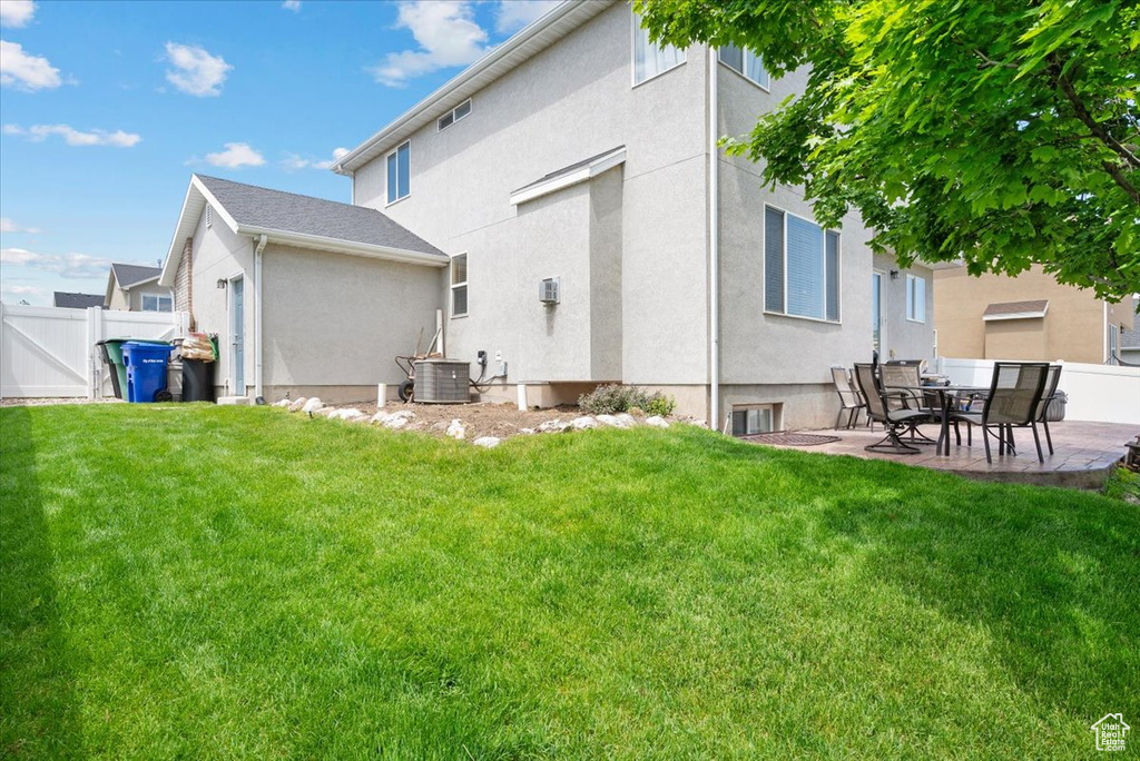 Rear view of property with a lawn, central AC unit, and a patio area