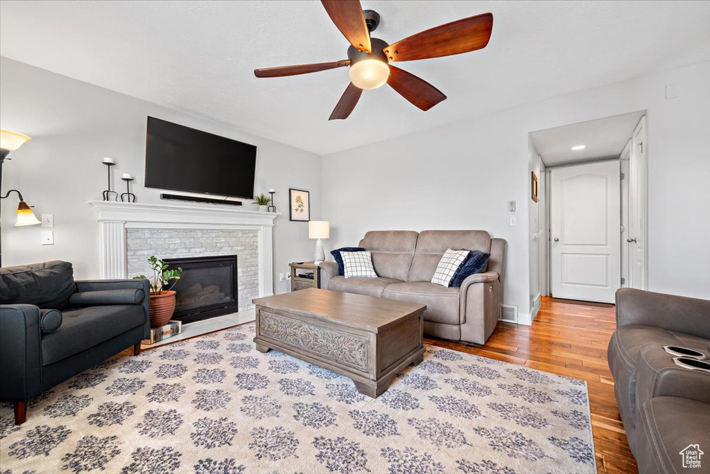 Living room with a stone fireplace, ceiling fan, and hardwood / wood-style floors