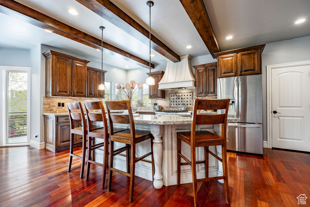 Kitchen with dark wood-type flooring, light stone counters, custom range hood, and stainless steel fridge with ice dispenser