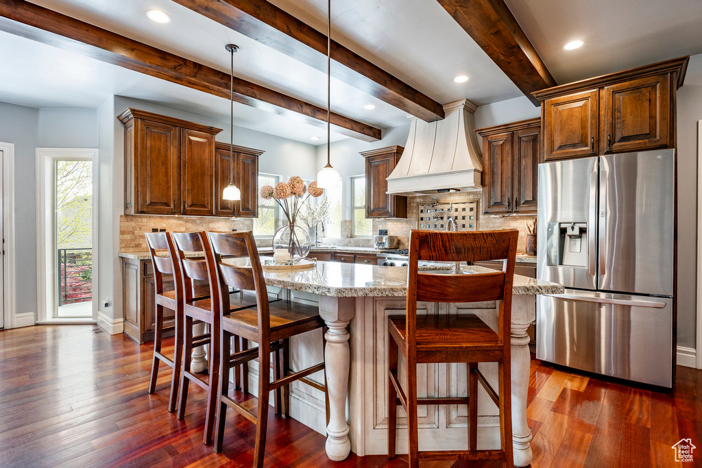 Kitchen featuring dark hardwood / wood-style floors, premium range hood, stainless steel refrigerator with ice dispenser, and beam ceiling