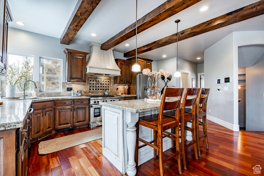 Kitchen featuring stainless steel appliances, custom exhaust hood, light stone countertops, and dark hardwood / wood-style flooring