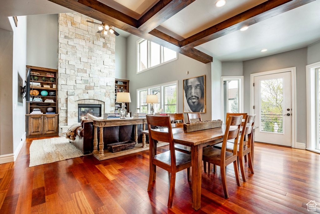 Dining room featuring a stone fireplace, ceiling fan, hardwood / wood-style floors, and beamed ceiling