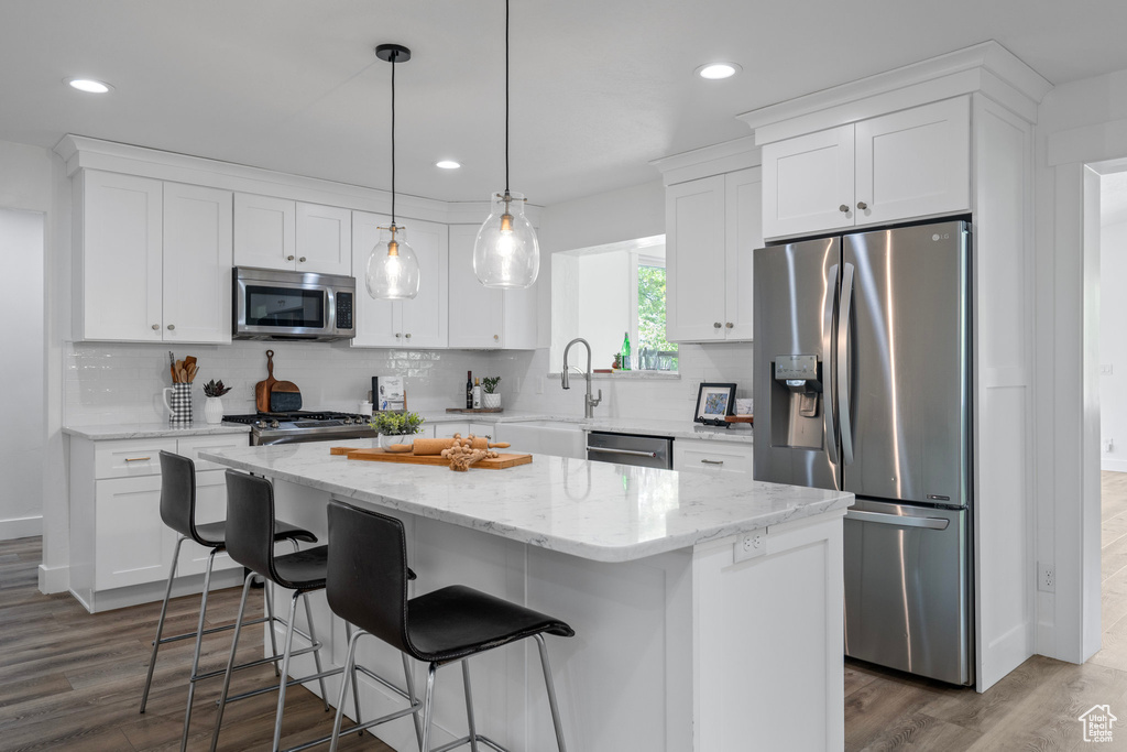 Kitchen with backsplash, wood-type flooring, a kitchen island, and appliances with stainless steel finishes