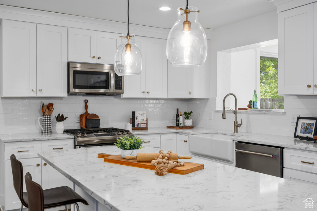 Kitchen featuring light stone countertops, white cabinets, backsplash, and appliances with stainless steel finishes