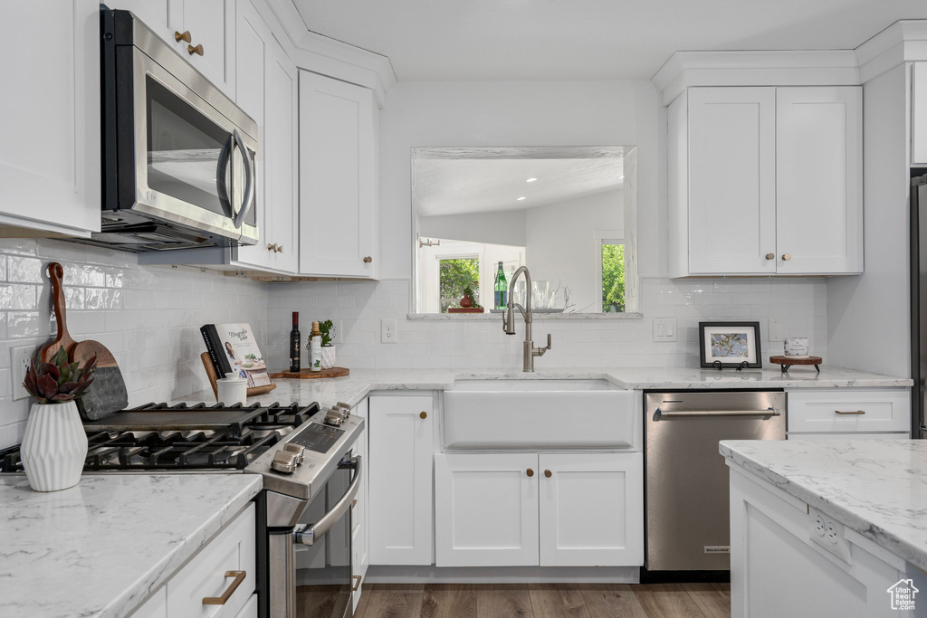 Kitchen with appliances with stainless steel finishes, hardwood / wood-style flooring, lofted ceiling, and backsplash