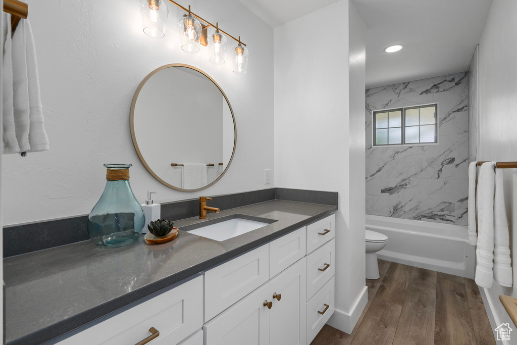 Full bathroom featuring hardwood / wood-style flooring, tiled shower / bath combo, vanity, and toilet