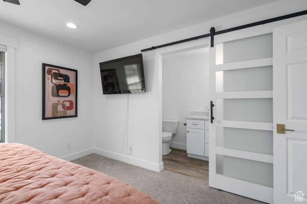 Unfurnished bedroom featuring a barn door, ceiling fan, connected bathroom, and hardwood / wood-style flooring