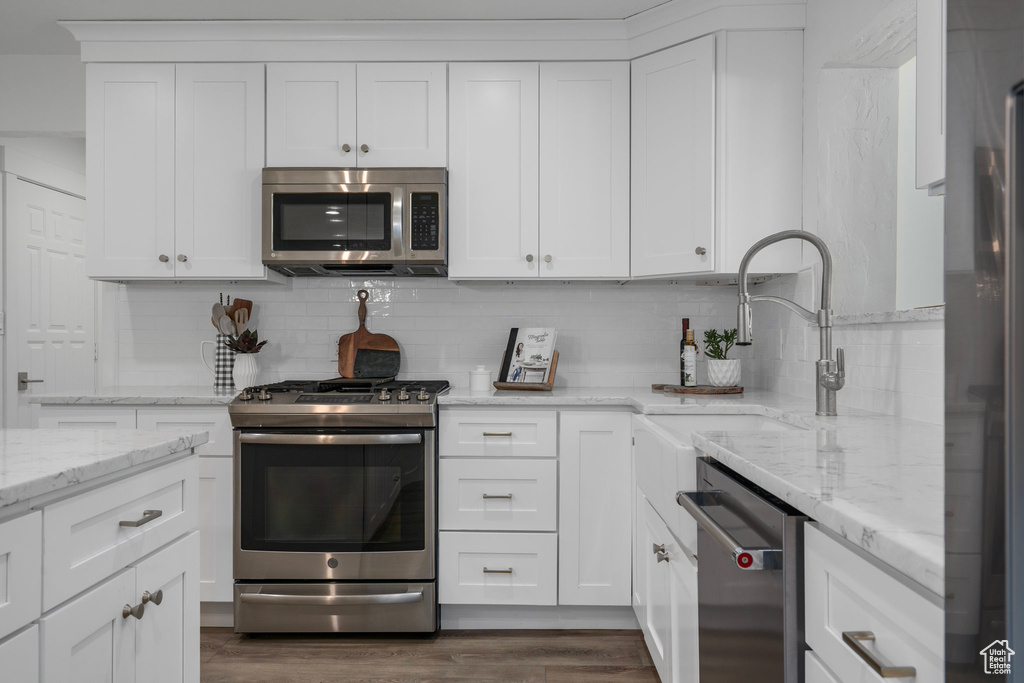 Kitchen featuring light stone countertops, dark wood-type flooring, backsplash, white cabinets, and appliances with stainless steel finishes