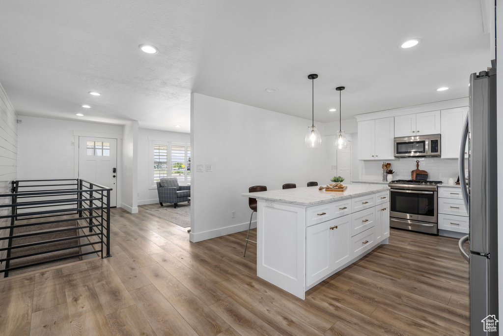 Kitchen featuring pendant lighting, wood-type flooring, a center island, white cabinetry, and appliances with stainless steel finishes