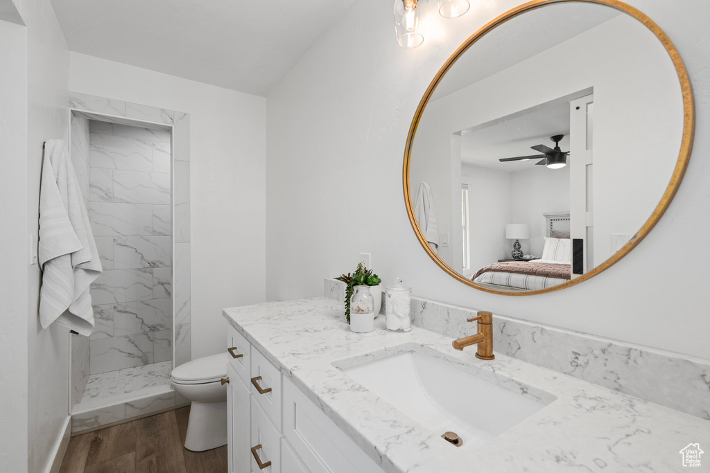 Bathroom with ceiling fan, a tile shower, hardwood / wood-style flooring, toilet, and vanity