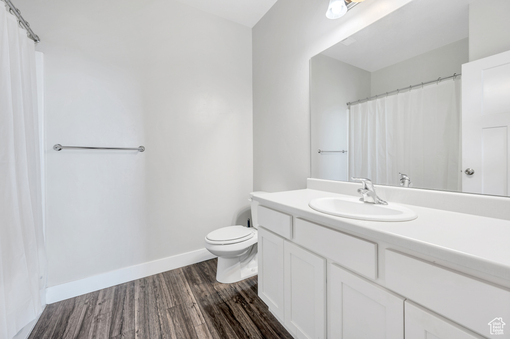 Bathroom with wood-type flooring, vanity with extensive cabinet space, and toilet