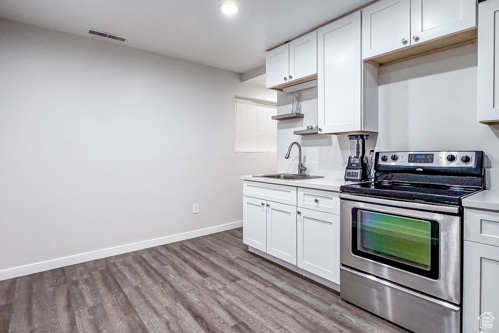 Kitchen with sink, white cabinets, wood-type flooring, and stainless steel range with electric cooktop