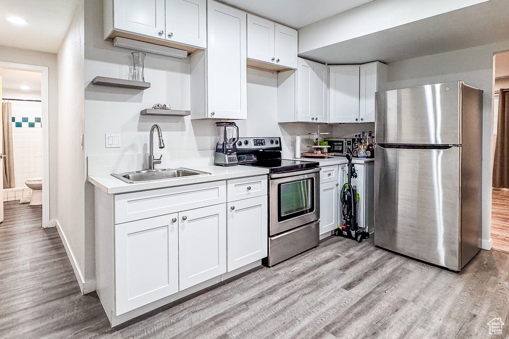 Kitchen with sink, stainless steel appliances, white cabinets, and light hardwood / wood-style flooring