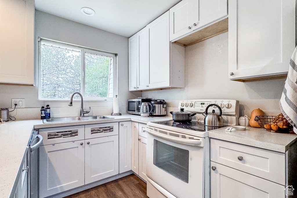 Kitchen featuring dark hardwood / wood-style flooring, stainless steel dishwasher, white electric range oven, white cabinets, and sink