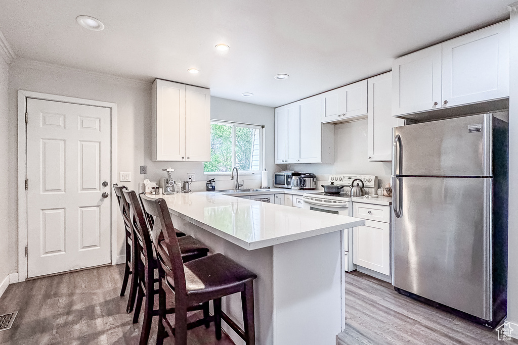 Kitchen featuring white electric range, stainless steel fridge, hardwood / wood-style flooring, a breakfast bar area, and sink