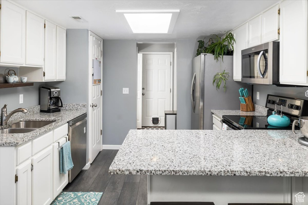 Kitchen with dark hardwood / wood-style floors, kitchen peninsula, sink, white cabinets, and appliances with stainless steel finishes