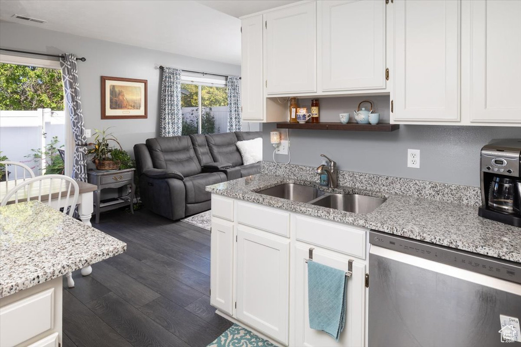 Kitchen with light stone counters, dark hardwood / wood-style flooring, stainless steel dishwasher, white cabinets, and sink