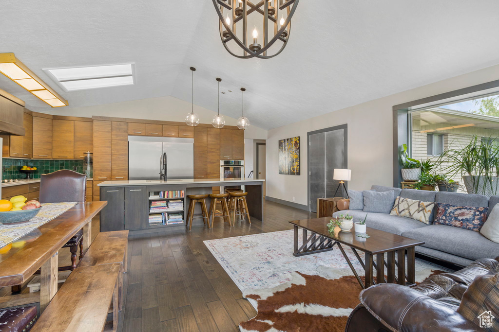 Living room featuring a chandelier, dark hardwood / wood-style floors, and vaulted ceiling with skylight