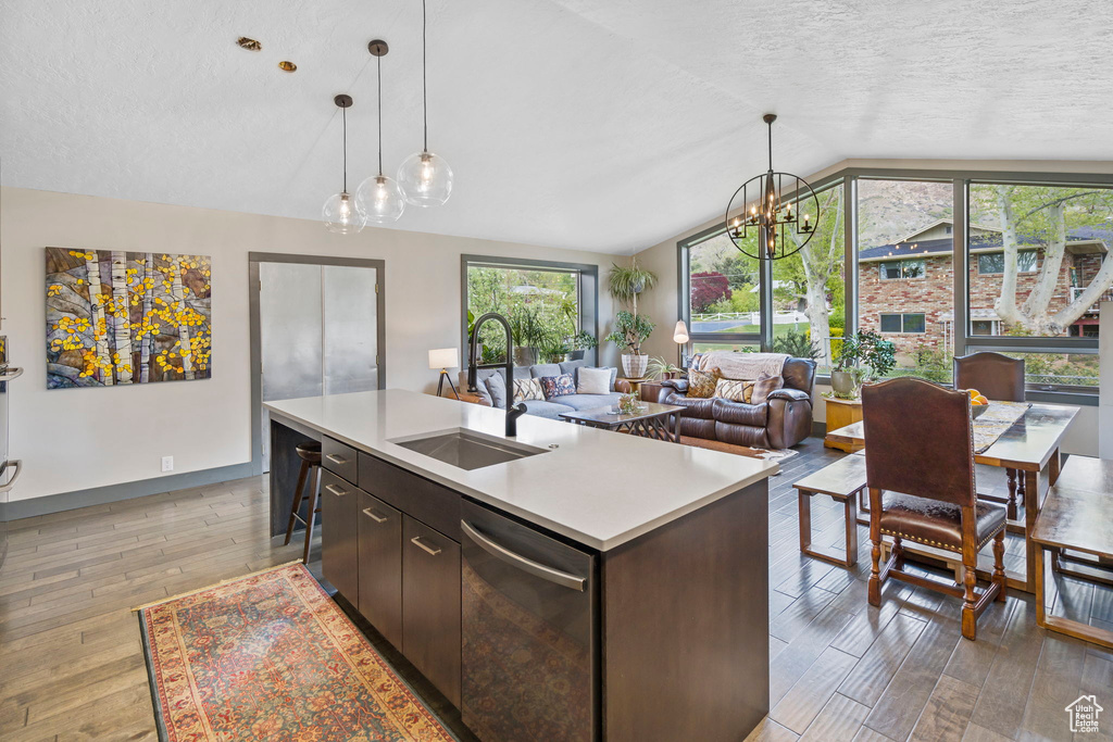 Kitchen with dishwasher, dark brown cabinets, lofted ceiling, hanging light fixtures, and light hardwood / wood-style flooring