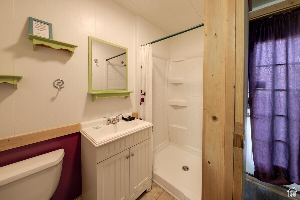 Bathroom featuring a shower with curtain, tile flooring, toilet, and vanity