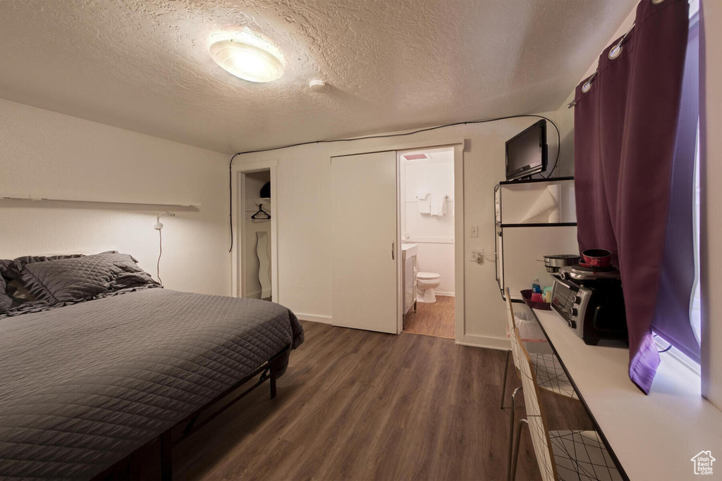 Bedroom with dark hardwood / wood-style flooring, a textured ceiling, and ensuite bath