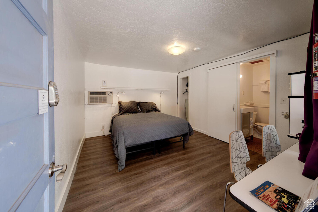 Bedroom featuring hardwood / wood-style floors, ensuite bath, an AC wall unit, and a textured ceiling