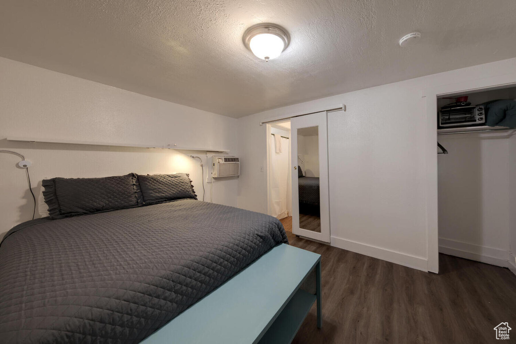 Bedroom featuring dark wood-type flooring, a closet, a textured ceiling, and a wall mounted air conditioner