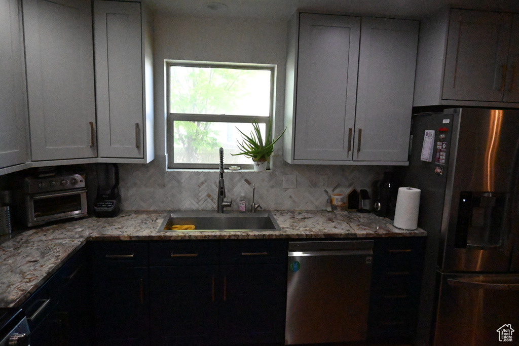 Kitchen featuring sink, tasteful backsplash, light stone counters, and stainless steel appliances