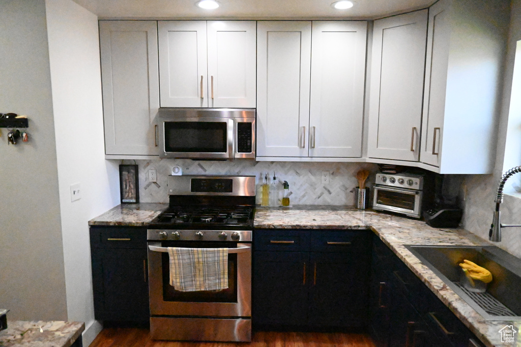 Kitchen featuring light stone countertops, tasteful backsplash, stainless steel appliances, dark hardwood / wood-style flooring, and sink