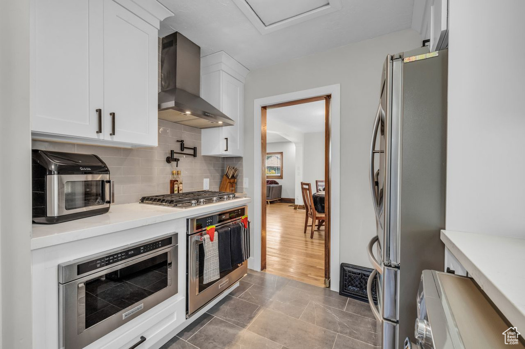 Kitchen featuring dark wood-type flooring, backsplash, wall chimney exhaust hood, white cabinetry, and appliances with stainless steel finishes