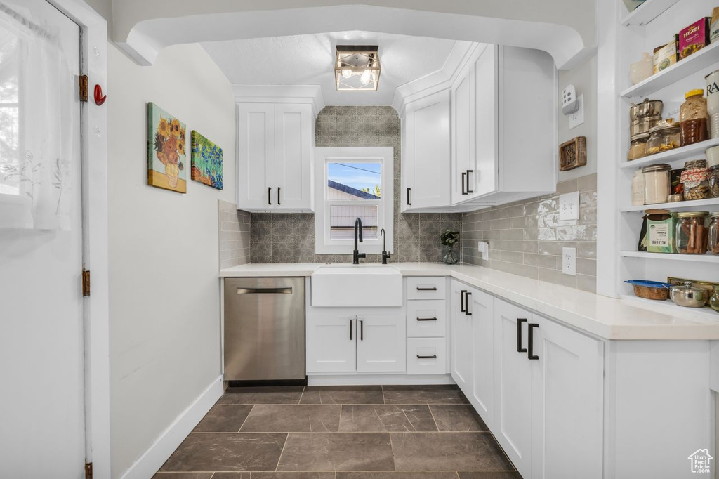 Kitchen featuring dark tile floors, dishwasher, backsplash, white cabinets, and sink