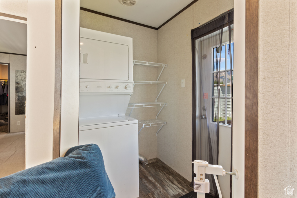 Laundry area featuring ornamental molding, stacked washer and dryer, and dark hardwood / wood-style floors