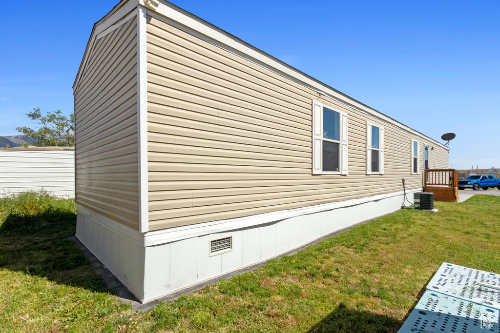 View of side of home with central AC unit and a yard